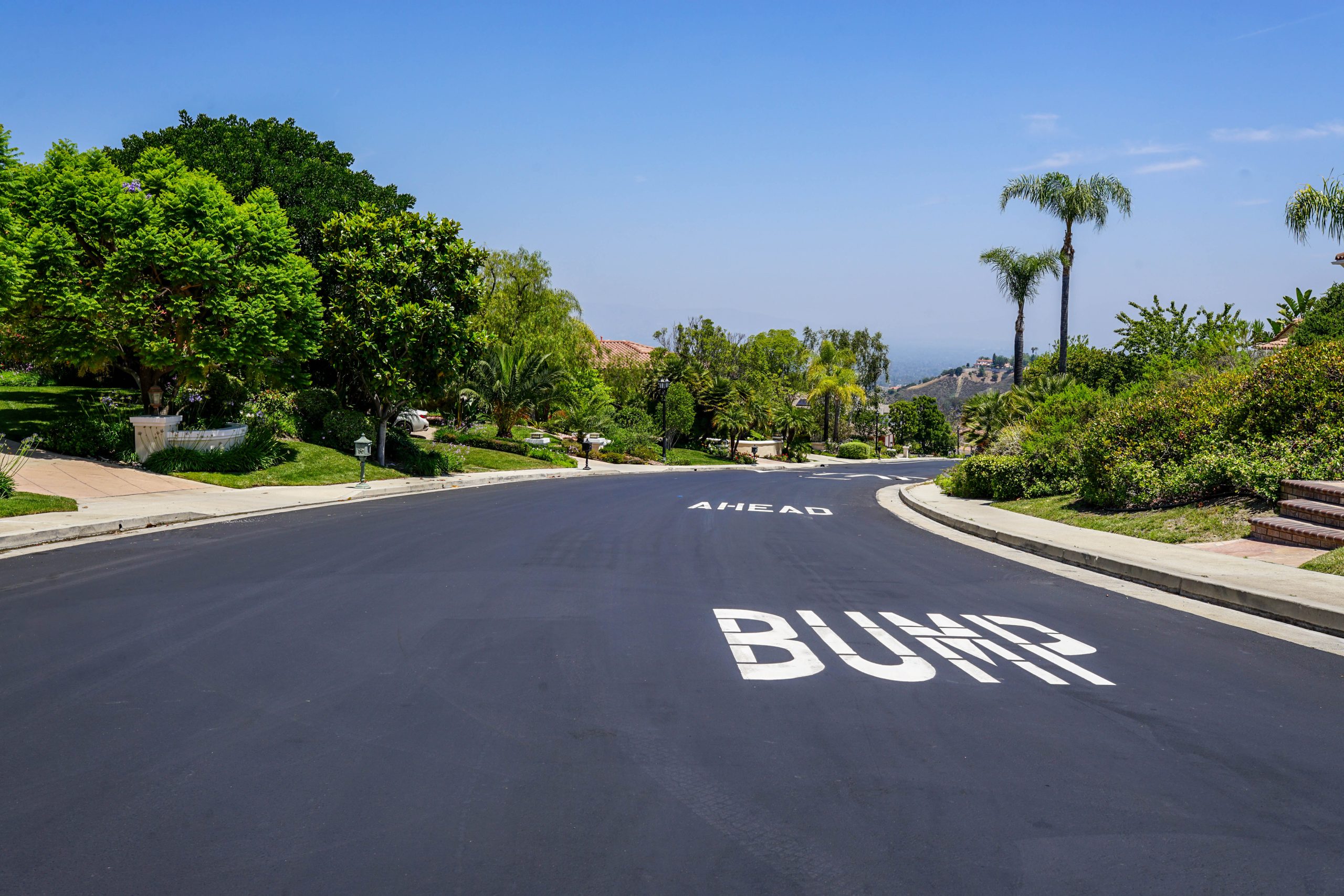 Asphalt roadway with bright “BUMP AHEAD” pavement striping in a Tarzana HOA community
