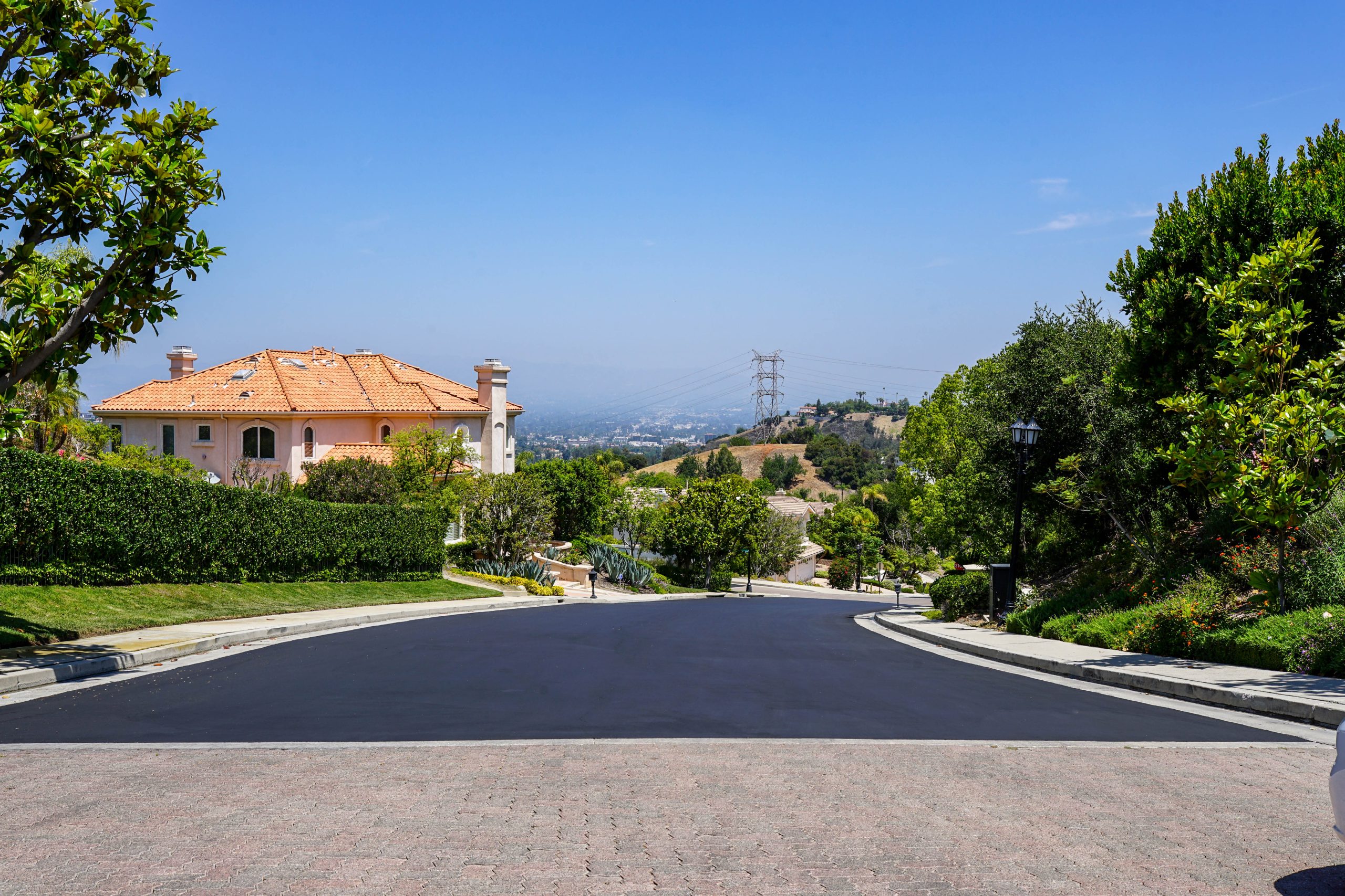Wide view of a newly sealcoated residential street with scenic hills and luxury homes in Tarzana