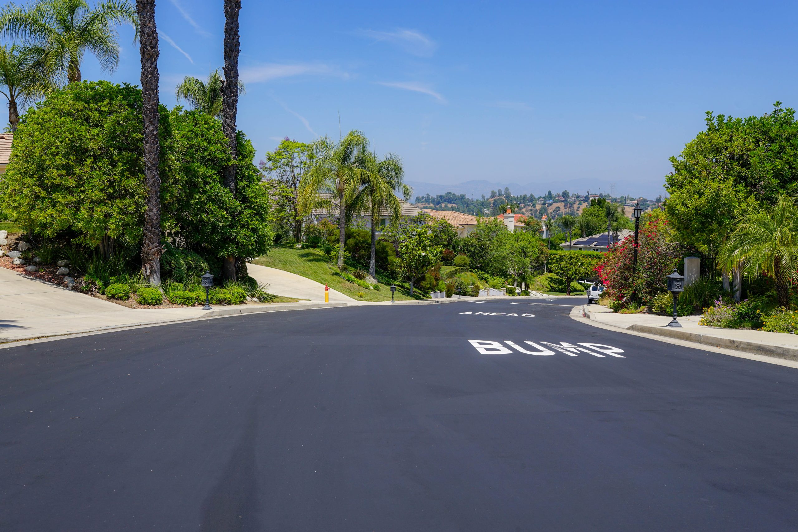 Smooth black asphalt on residential street with clear “BUMP AHEAD” striping after sealcoating